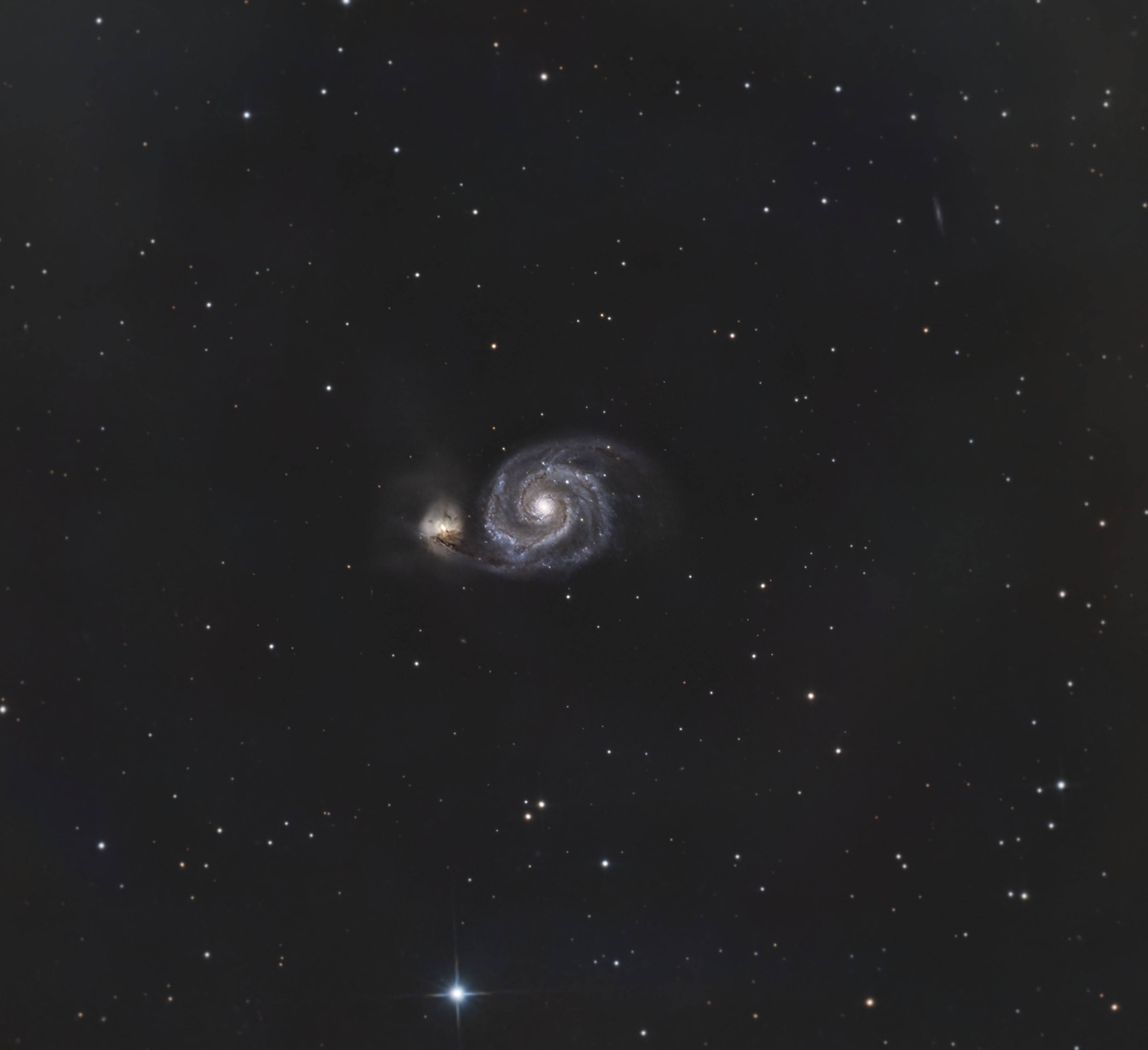 The Whirlpool Galaxy (M51) interacting with its smaller companion, showing bright spiral arms filled with blue star clusters and pink nebulae, against a dark background of distant galaxies.